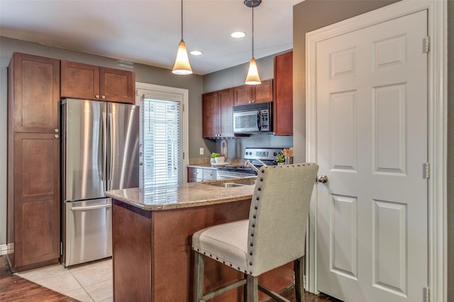 kitchen featuring light tile patterned floors, a breakfast bar area, light stone countertops, pendant lighting, and appliances with stainless steel finishes