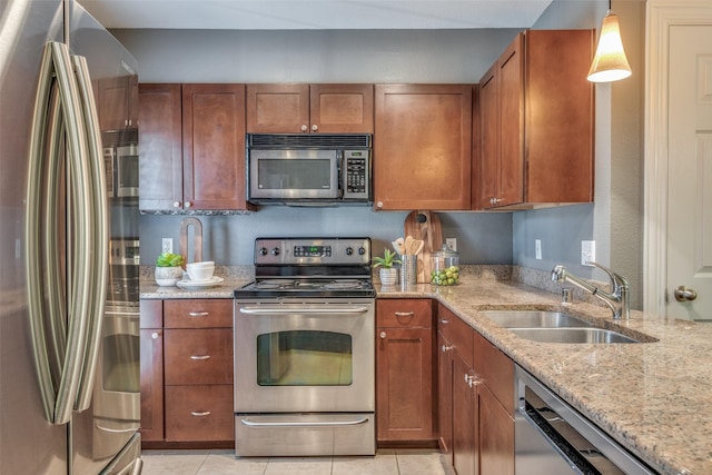 kitchen with light stone countertops, decorative light fixtures, stainless steel appliances, light tile patterned floors, and sink