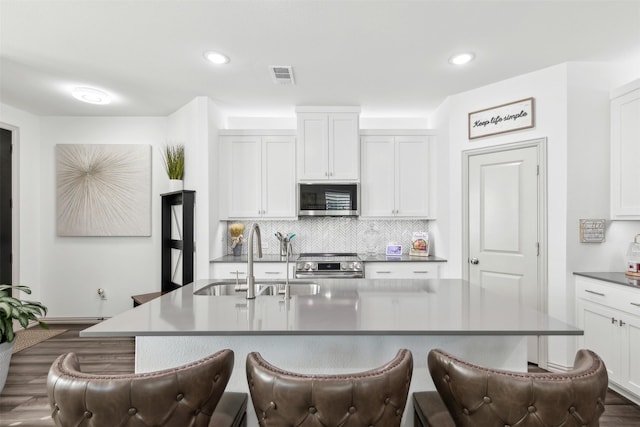 kitchen with appliances with stainless steel finishes, white cabinetry, decorative backsplash, sink, and a center island with sink