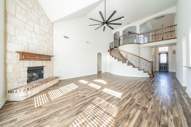 unfurnished living room featuring a high ceiling, ceiling fan, a stone fireplace, and hardwood / wood-style flooring