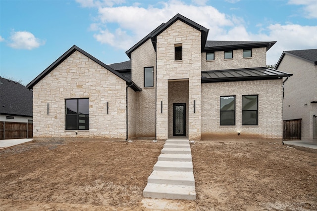 view of front facade with metal roof, brick siding, a standing seam roof, and fence