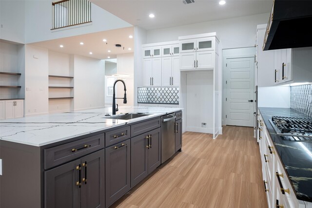 kitchen featuring stainless steel appliances, light hardwood / wood-style floors, white cabinets, and a center island with sink