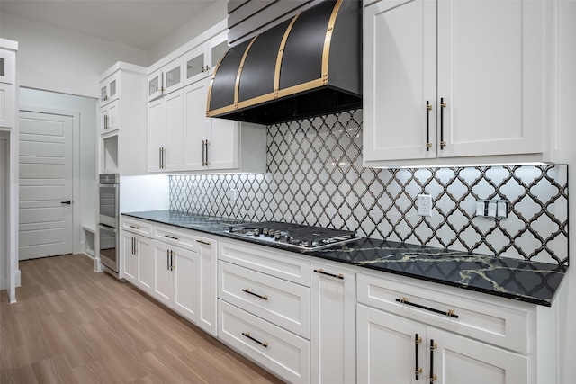 kitchen featuring tasteful backsplash, white cabinetry, dark stone counters, stainless steel gas stovetop, and exhaust hood