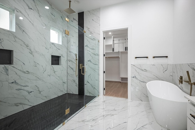 bathroom featuring a marble finish shower, marble tiled floors, a freestanding bath, tile walls, and stone wall