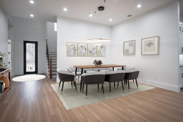 dining room featuring stairway, baseboards, wood finished floors, recessed lighting, and a high ceiling
