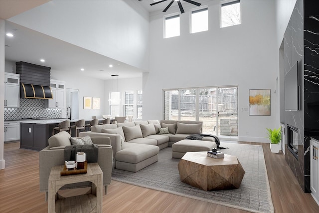 living room with ceiling fan, a towering ceiling, wood finished floors, recessed lighting, and baseboards