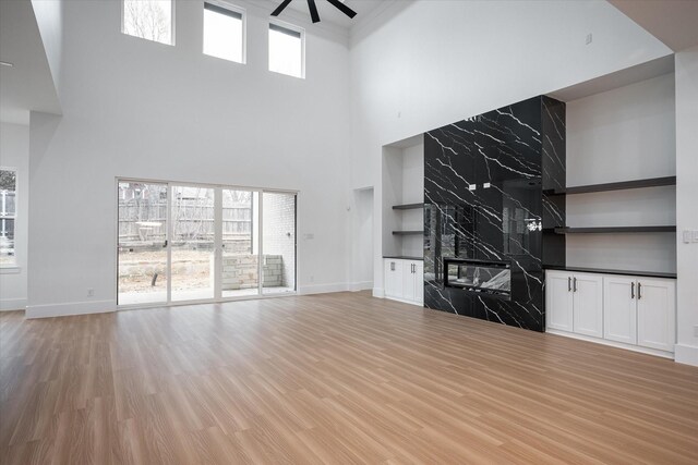 unfurnished living room with ceiling fan, a high ceiling, light wood-type flooring, a fireplace, and baseboards