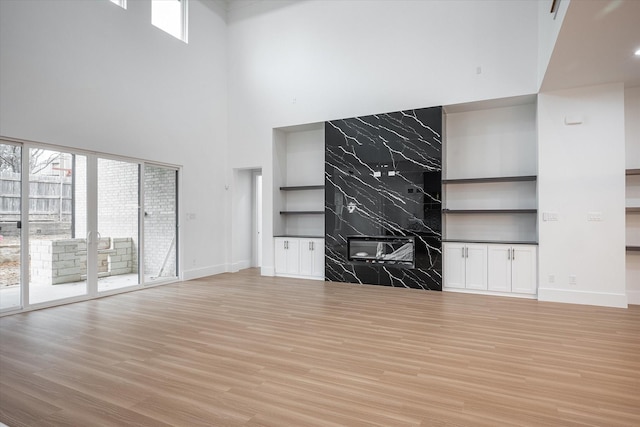 unfurnished living room featuring a towering ceiling, light wood-style flooring, baseboards, and plenty of natural light