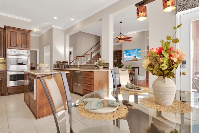 kitchen featuring light tile patterned floors, light stone countertops, stainless steel appliances, ornamental molding, and brown cabinets