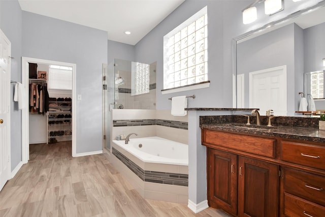 bathroom with wood finished floors, vanity, a spacious closet, a jetted tub, and a shower stall