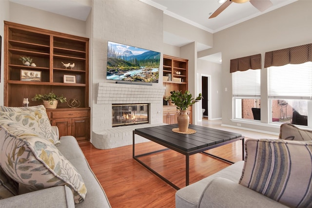 living room with crown molding, light wood-type flooring, ceiling fan, a fireplace, and a high ceiling