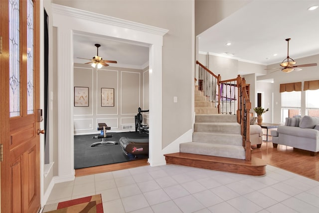 tiled foyer featuring ceiling fan, crown molding, and stairs