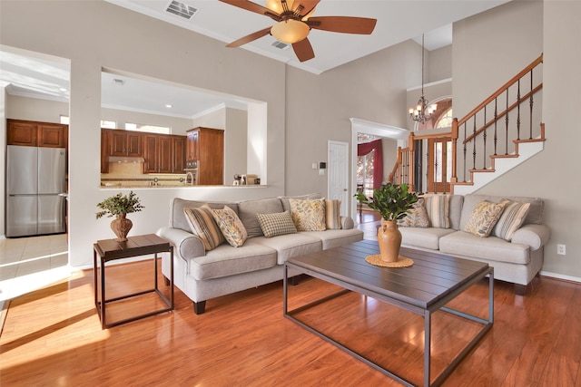 living room featuring crown molding, a towering ceiling, ceiling fan with notable chandelier, and light wood-type flooring