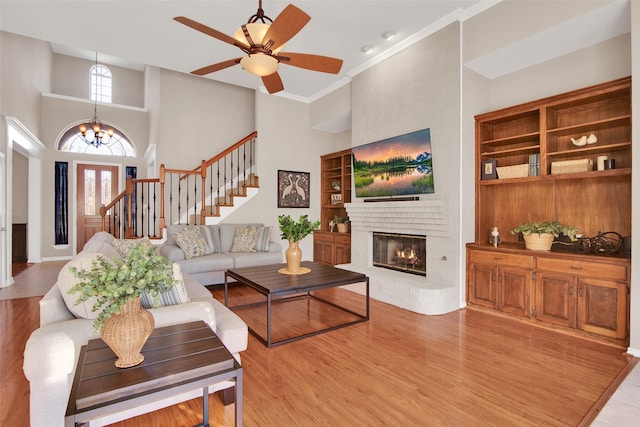 living area with stairway, a brick fireplace, wood finished floors, and a towering ceiling