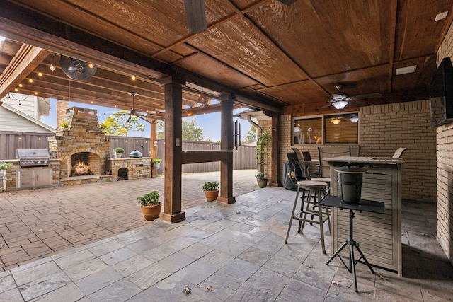 view of patio / terrace featuring grilling area, exterior kitchen, an outdoor stone fireplace, ceiling fan, and a bar