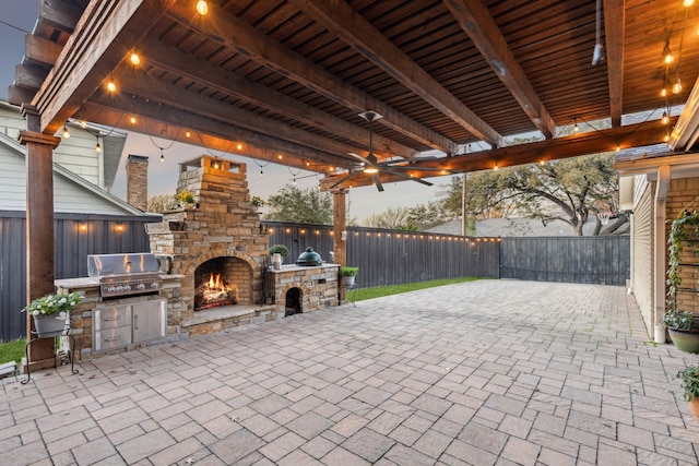 patio terrace at dusk featuring exterior kitchen, area for grilling, and an outdoor stone fireplace