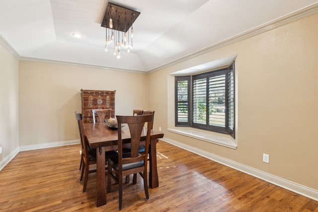 dining space with a notable chandelier, hardwood / wood-style floors, lofted ceiling, a tray ceiling, and crown molding