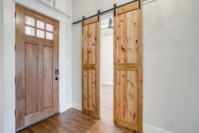 entryway with a barn door, wood finished floors, and baseboards