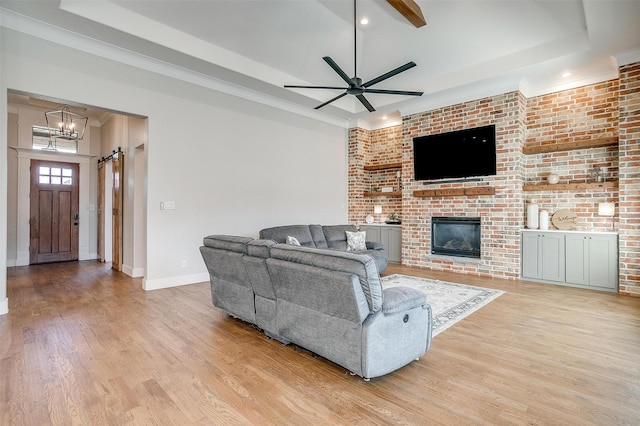 living area featuring ceiling fan with notable chandelier, a fireplace, baseboards, light wood finished floors, and a raised ceiling