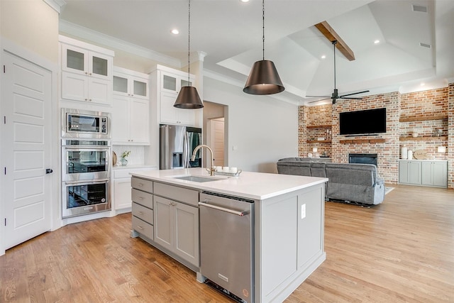 kitchen with a fireplace, appliances with stainless steel finishes, a kitchen island with sink, a sink, and light wood-type flooring