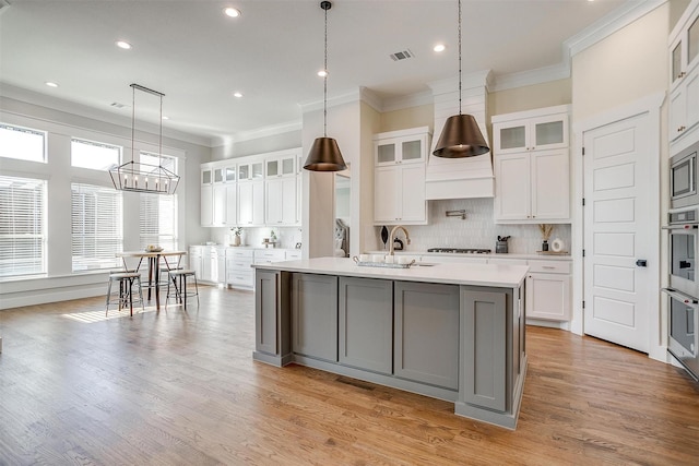 kitchen featuring visible vents, light countertops, ornamental molding, backsplash, and a center island with sink