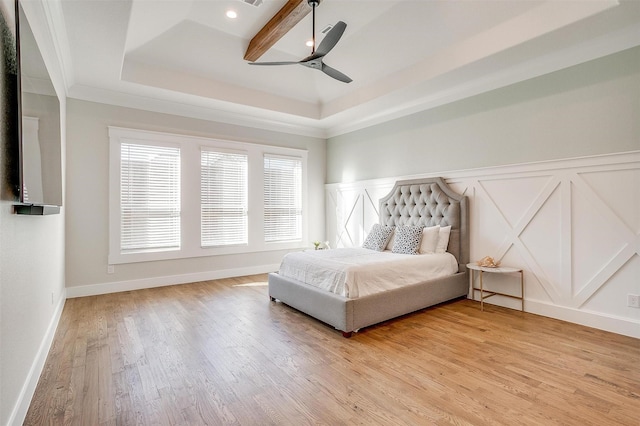 bedroom featuring a tray ceiling, a wainscoted wall, crown molding, light wood finished floors, and a decorative wall