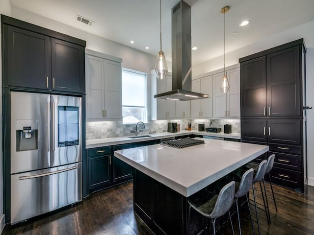 kitchen with appliances with stainless steel finishes, hanging light fixtures, a kitchen island, island range hood, and dark wood-type flooring