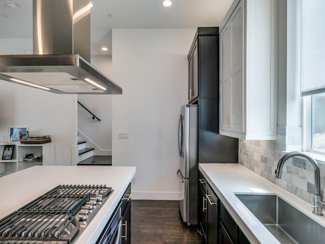 kitchen with dark hardwood / wood-style floors, island exhaust hood, backsplash, appliances with stainless steel finishes, and sink