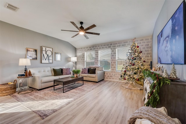 living room with brick wall, ceiling fan, vaulted ceiling, and light hardwood / wood-style flooring