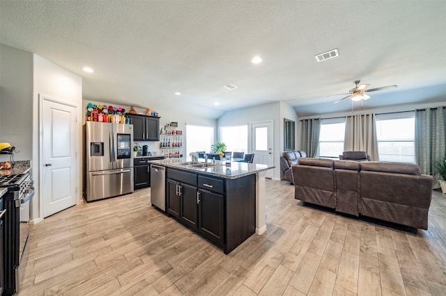 kitchen featuring an island with sink, a textured ceiling, appliances with stainless steel finishes, and a healthy amount of sunlight