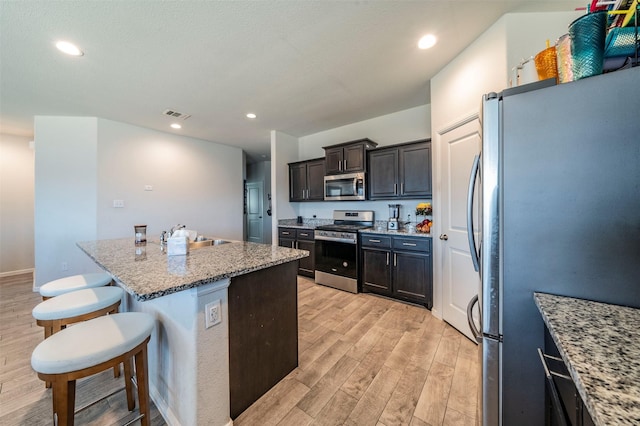 kitchen with a breakfast bar area, a center island with sink, stainless steel appliances, light stone counters, and sink