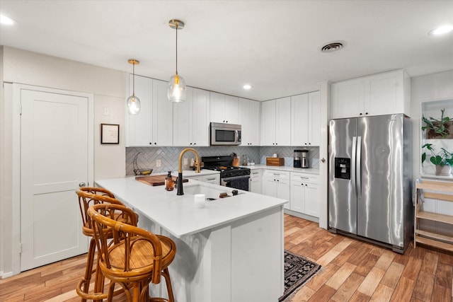 kitchen with pendant lighting, white cabinets, appliances with stainless steel finishes, a kitchen bar, and kitchen peninsula