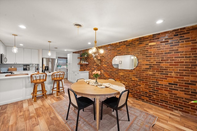 dining space with brick wall and light hardwood / wood-style flooring