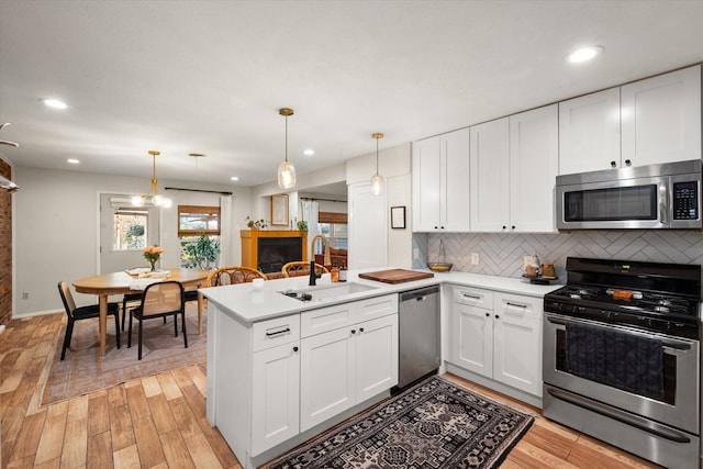 kitchen with white cabinetry, hanging light fixtures, appliances with stainless steel finishes, and kitchen peninsula