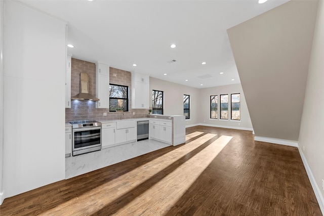 kitchen featuring white cabinets, wall chimney exhaust hood, hardwood / wood-style floors, decorative backsplash, and appliances with stainless steel finishes