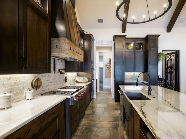 kitchen with premium range hood, backsplash, stainless steel gas cooktop, light stone countertops, and beam ceiling