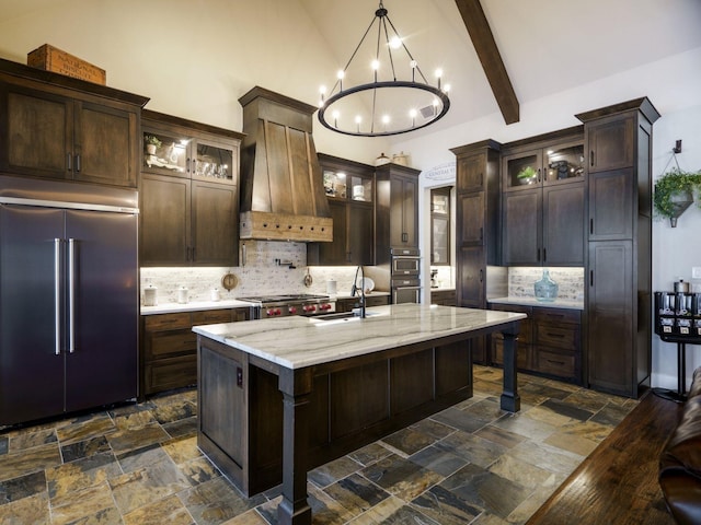 kitchen featuring sink, appliances with stainless steel finishes, a kitchen island with sink, custom exhaust hood, and beamed ceiling