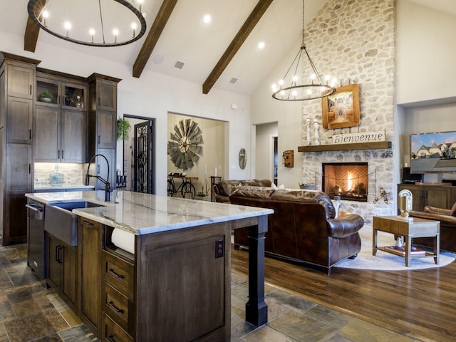 kitchen with an inviting chandelier, hanging light fixtures, high vaulted ceiling, dark brown cabinetry, and an island with sink