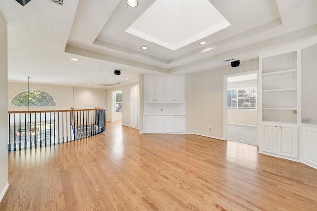 unfurnished room featuring a raised ceiling, built in features, and a wealth of natural light