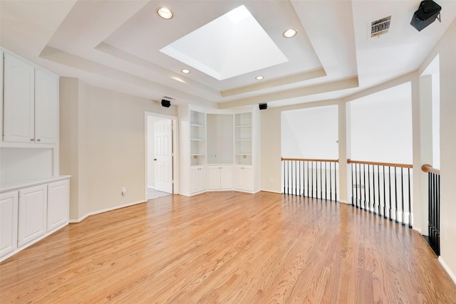 empty room featuring light hardwood / wood-style floors, built in features, and a tray ceiling