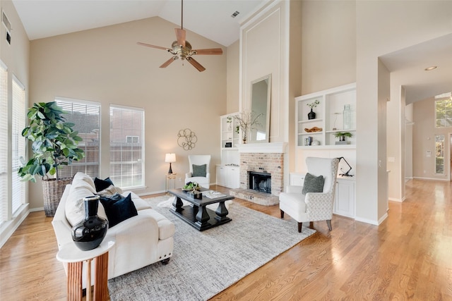 living room with high vaulted ceiling, a brick fireplace, ceiling fan, and light wood-type flooring