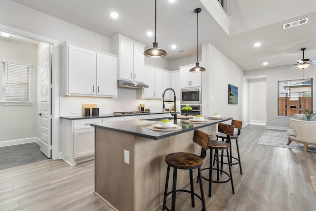 kitchen featuring a breakfast bar, light wood finished floors, tasteful backsplash, dark countertops, and visible vents