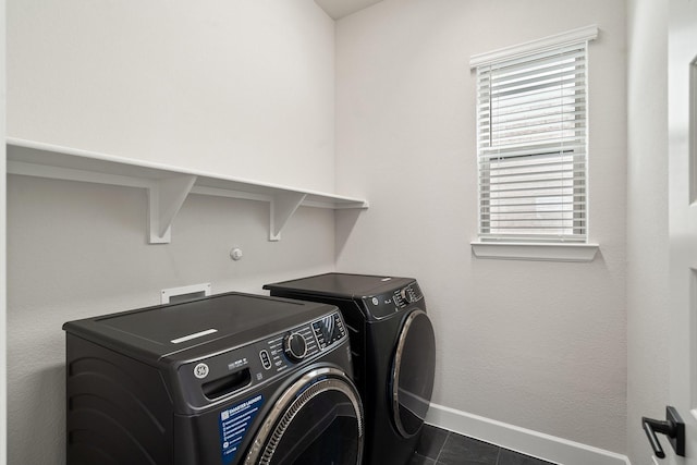 washroom with washer and clothes dryer, dark tile patterned floors, and a wealth of natural light