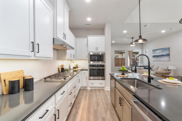 kitchen with stainless steel appliances, sink, white cabinets, light wood-type flooring, and hanging light fixtures