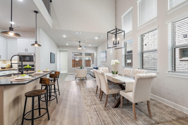 dining space with a high ceiling, light hardwood / wood-style flooring, and ceiling fan with notable chandelier