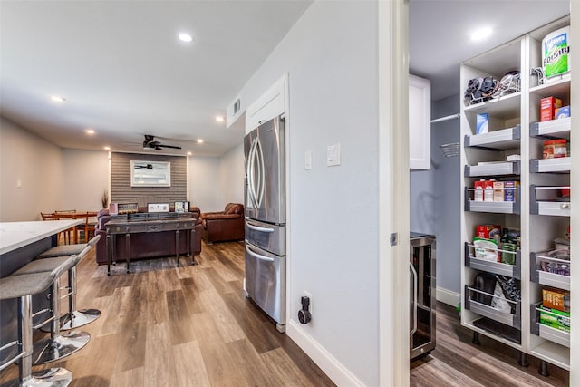 kitchen featuring wood-type flooring, ceiling fan, white cabinetry, and stainless steel refrigerator