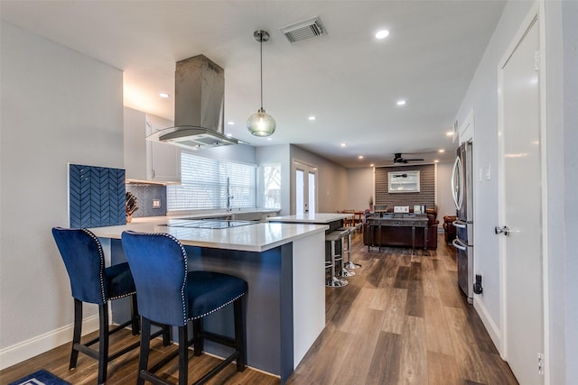 kitchen featuring kitchen peninsula, hanging light fixtures, island exhaust hood, a breakfast bar area, and white cabinets