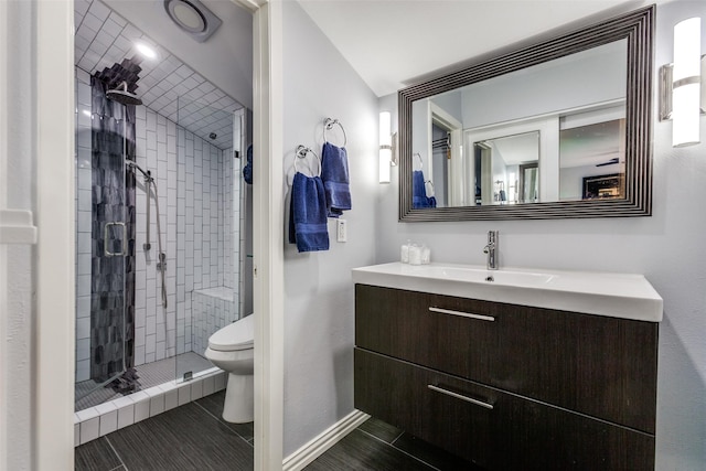 bathroom with toilet, a tile shower, and vanity