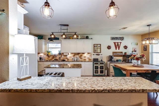 kitchen with sink, white cabinets, backsplash, hanging light fixtures, and light stone countertops