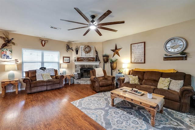 living room featuring a brick fireplace, dark hardwood / wood-style floors, and ceiling fan